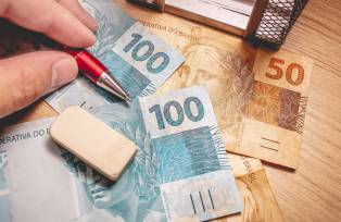 Real - Brazilian Currency. Money bills on a wooden table and a man holding a pen.