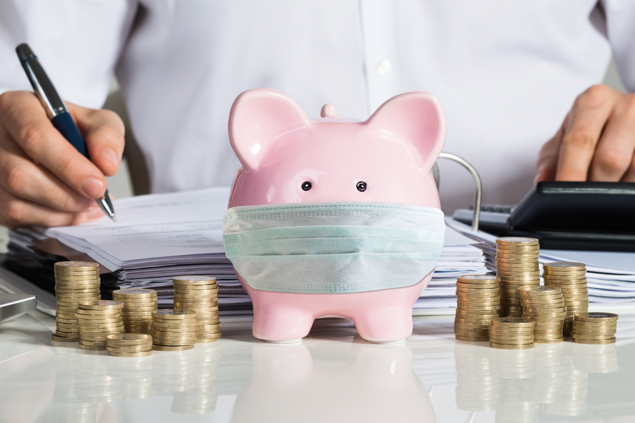 Businessman Calculating Invoice With Piggybank And Coins At Desk