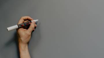 Mão segura caneta, que escreve em quadro em branco.