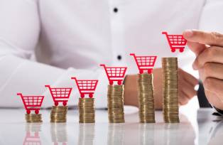 Businessperson placing shopping cart over stacked coins