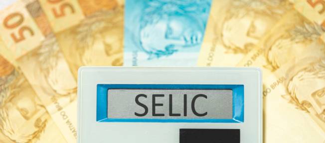 Foto de stock de As iniciais SELIC referem-se à taxa básica de juros no Brasil escritas na exibição de uma calculadora com notas de reais na composição. Economia e investimentos brasileiros.