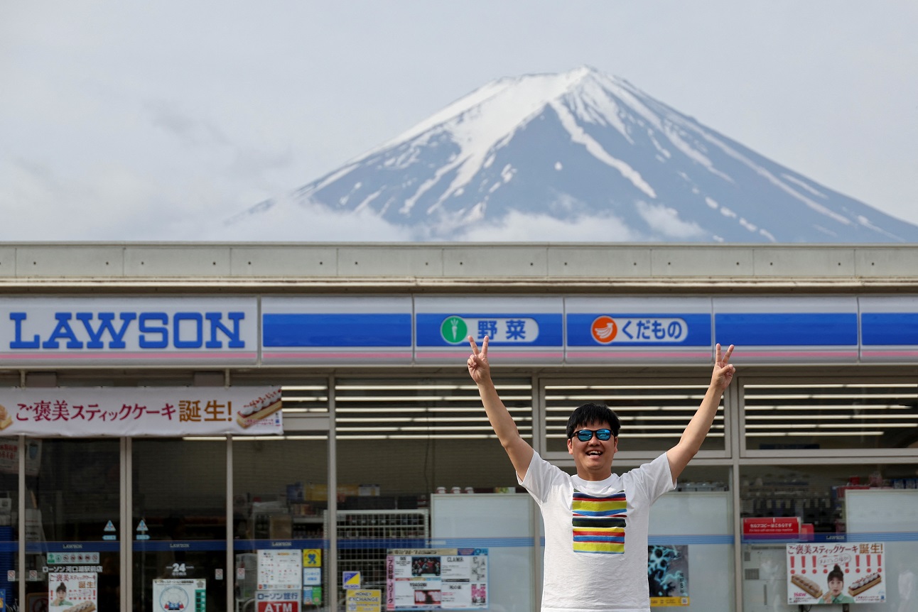 Um turista posa para uma foto do Monte Fuji aparecendo em uma loja de conveniência na cidade de Fujikawaguchiko, província de Yamanashi, Japão, 21 de maio de 2024 (REUTERS/Kim Kyung-Hoon)