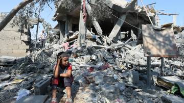 Uma criança senta-se em meio aos escombros enquanto palestinos inspecionam uma casa destruída em um ataque israelense, durante o conflito entre Israel e Hamas, no campo de refugiados de Nusairat, na Faixa de Gaza central, em 9 de julho de 2024. REUTERS/Ramadan Abed