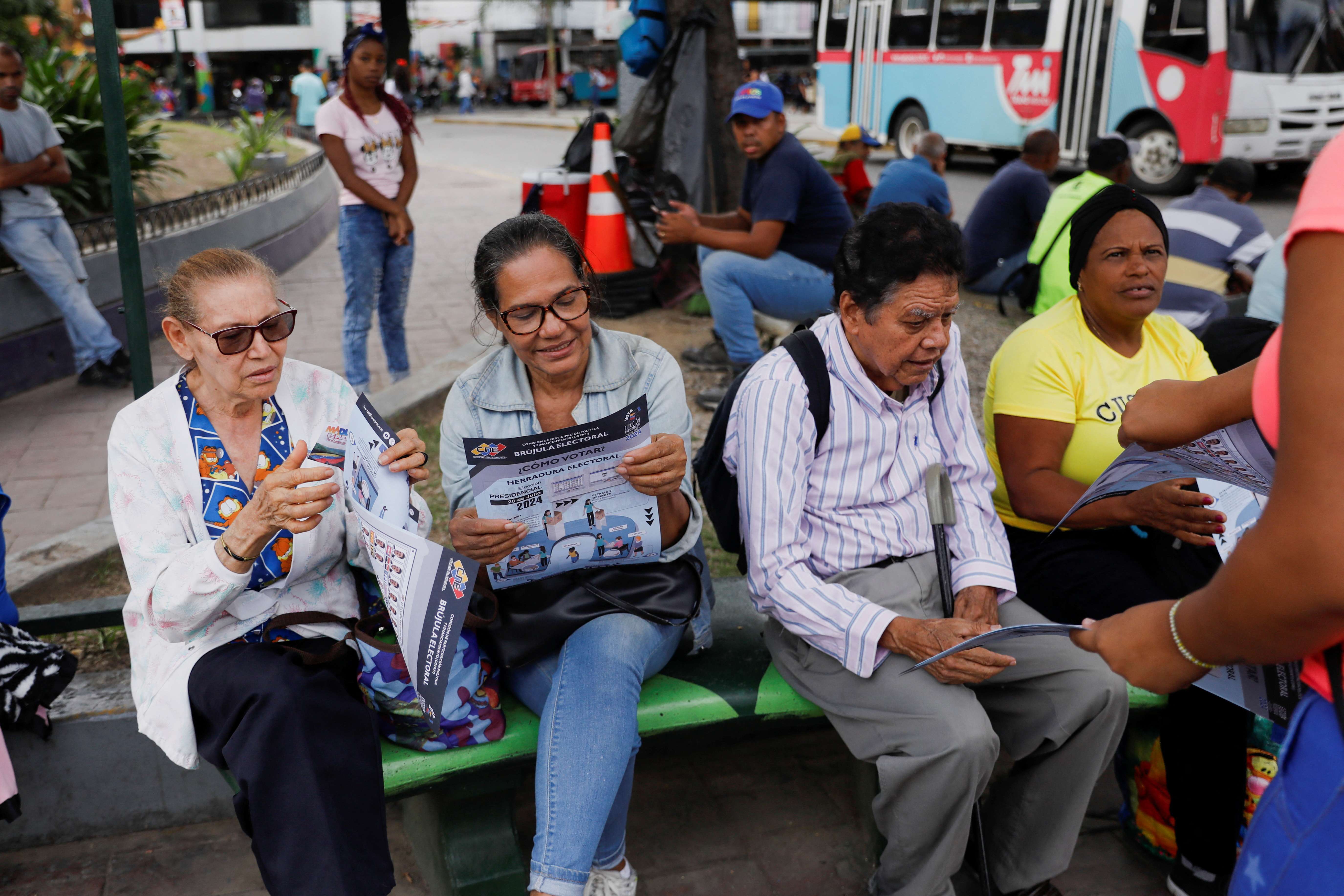 Pessoas olham folheto do boletim eleitoral para eleições presidenciais em Caracas - 17/7/2024 (Foto: Leonardo Fernandez Viloria/Reuters)