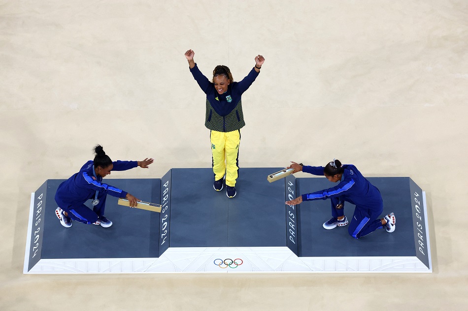 A medalhista de ouro Rebeca Andrade do Brasil comemora com a medalhista de prata Simone Biles dos Estados Unidos e o medalhista de bronze Jordan Chiles dos Estados Unidos no pódio. REUTERS/Athit Perawongmetha