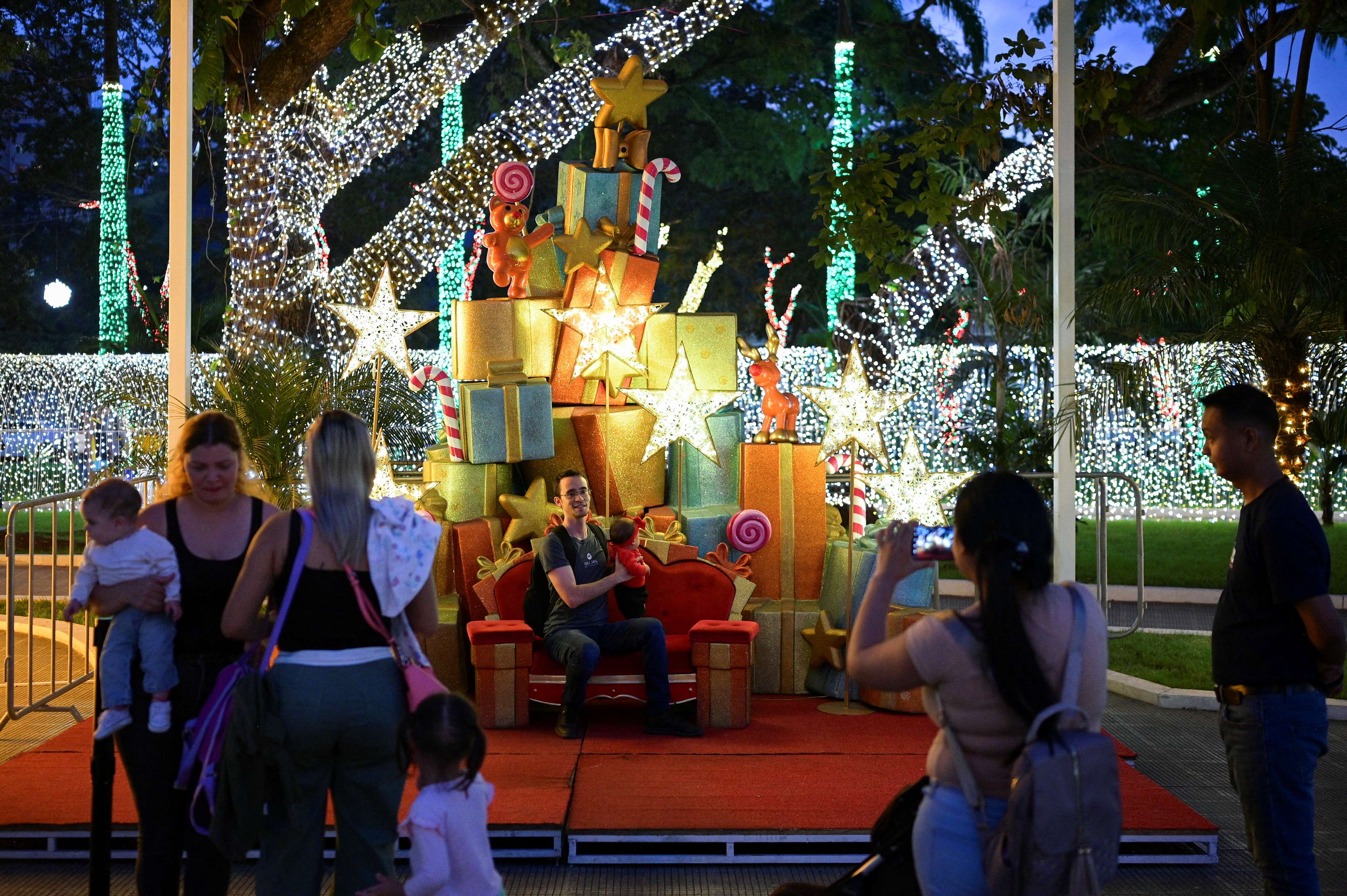 Famílias fazem fotos em frente às decorações de Natal em uma praça pública de Caracas, na Venezuela - 01/10/2024 (Foto: Gaby Oraa/Reuters)