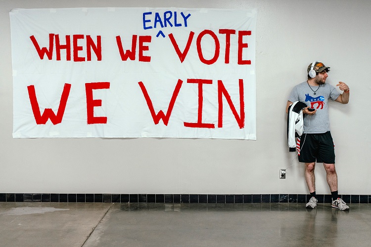 Homem em frente a um banner em um evento de campanha em Madison, Wisconsin, em 22 de outubro de 2024 (Jamie Kelter Davis/The New York Times)