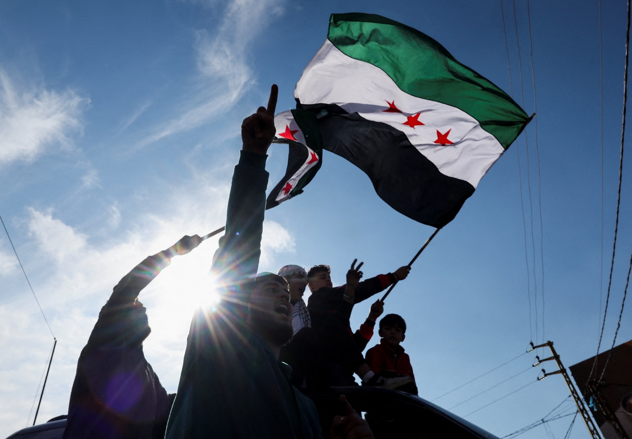 Uma pessoa agita uma bandeira da oposição síria, enquanto outras celebram no Atravessamento Fronteiriço de Masnaa, após os rebeldes sírios anunciarem que destituíram o presidente Bashar al-Assad, em 8 de dezembro de 2024 (Foto: REUTERS/Amr Abdallah Dalsh)