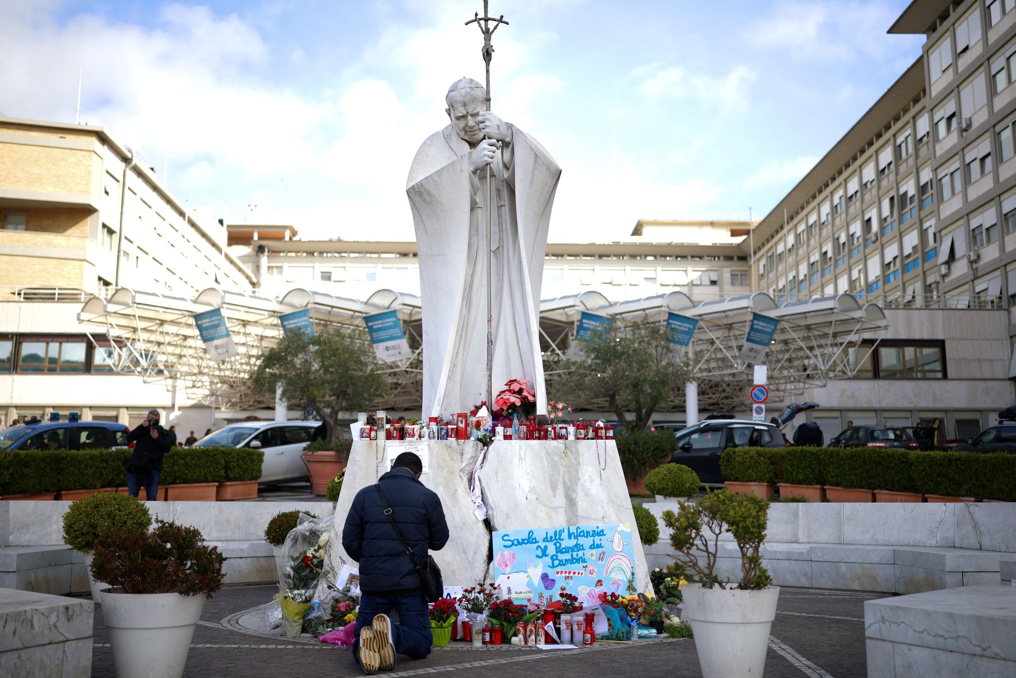 Homem reza perto de estátua do papa João Paulo 2º no Hospital Gemelli, em Roma 28/2/2025 (Foto: REUTERS/Alkis Konstantinidis)