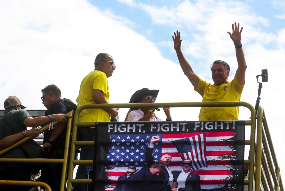 Jair Bolsonaro acena acima de uma faixa com uma imagem do presidente dos EUA, Donald Trump, enquanto manifestantes se reúnem para apoiá-lo na praia de Copacabana, no Rio de Janeiro, Brasil, 16 de março de 2025. (REUTERS/Pilar Olivares)